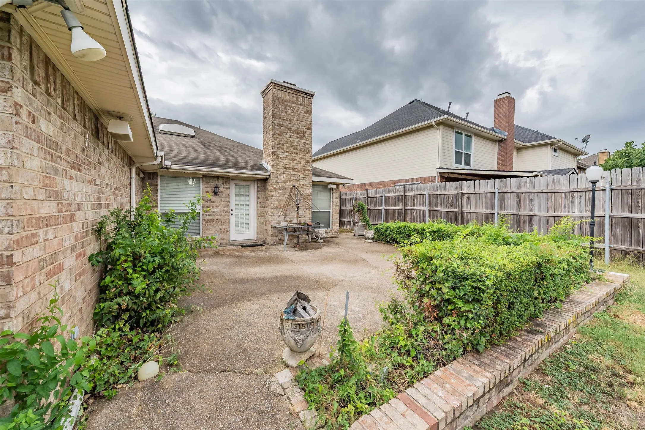 Brick exterior, concrete patio, brick chimney, privacy fence, mature landscaping