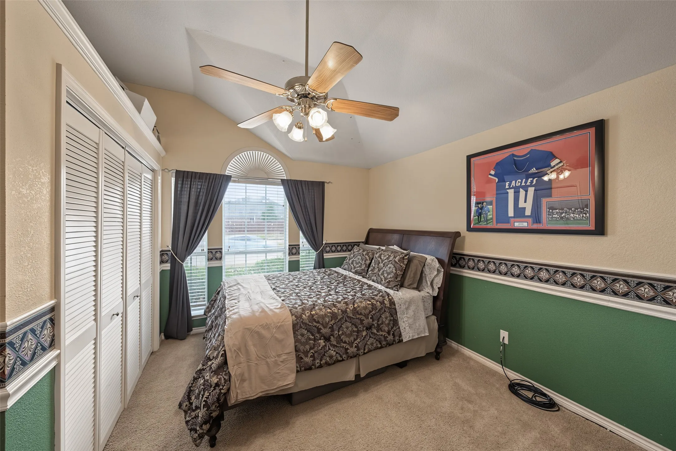 Vaulted ceiling with an attached fan light fixture, louvered closet doors, arched window with a transom, and carpeted flooring