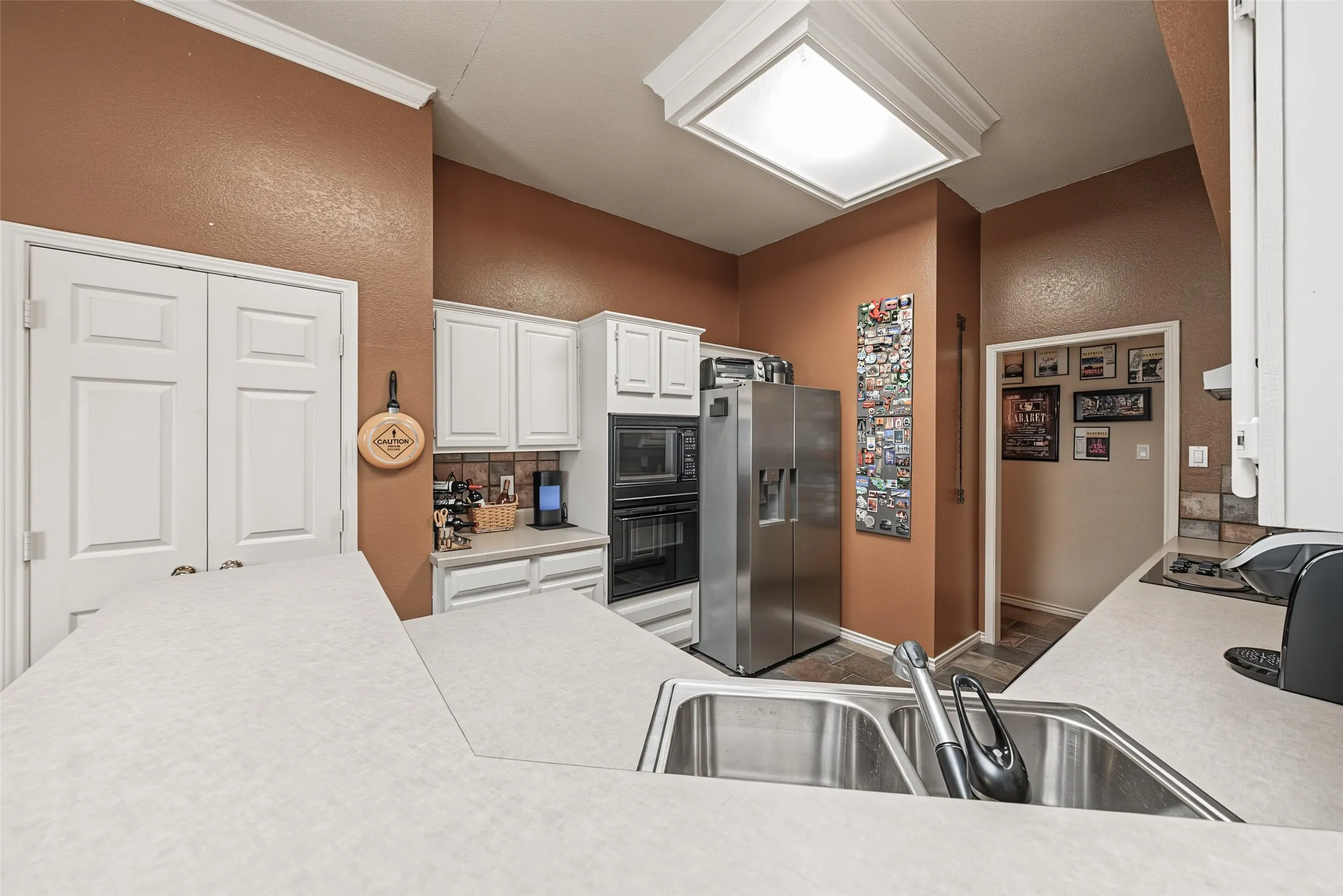 Stainless steel double basin sink with a single-handle faucet, white cabinetry, integrated stainless steel double oven, and a built-in refrigerator