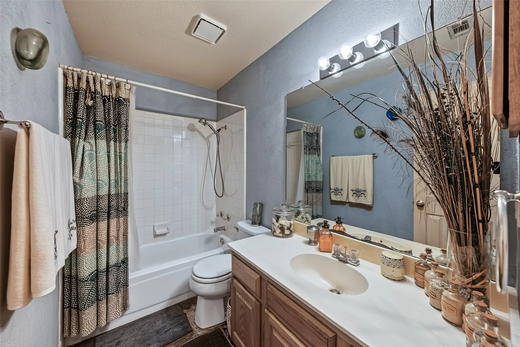 Full bathroom featuring a single vanity with an integrated sink, wood-finish cabinetry, a large wall-mounted mirror, and a bathtub with an overhead shower