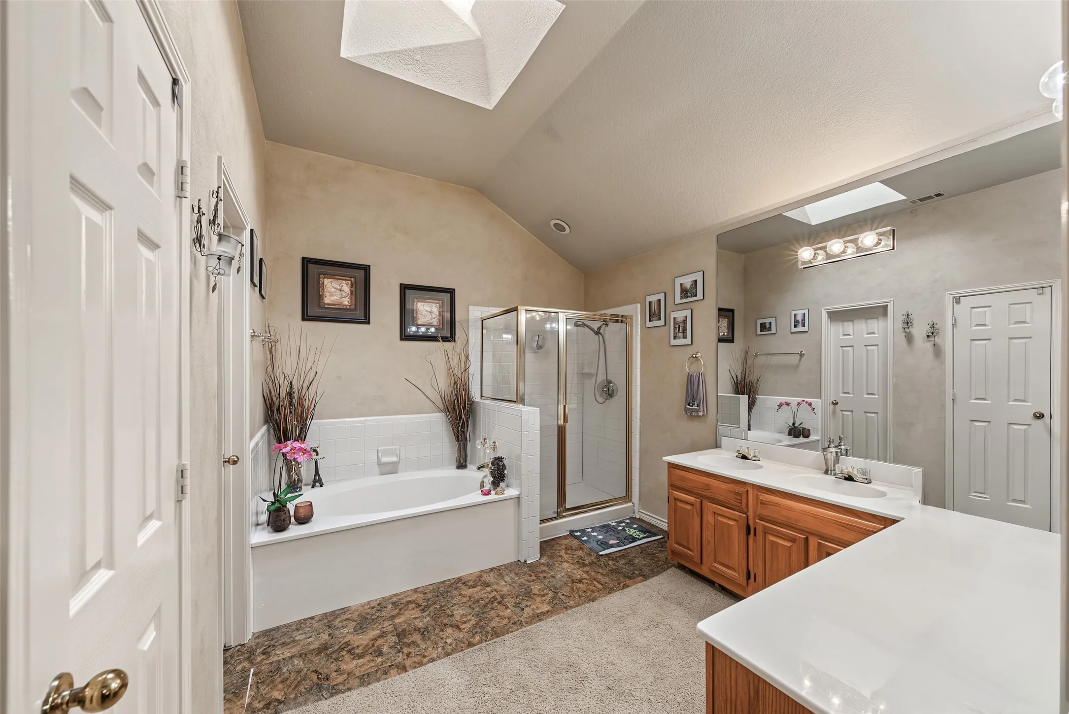 Dual skylights, vaulted ceiling, built-in soaking tub with tile surround, glass-enclosed shower, and a dual-sink vanity with wood-finish cabinetry
