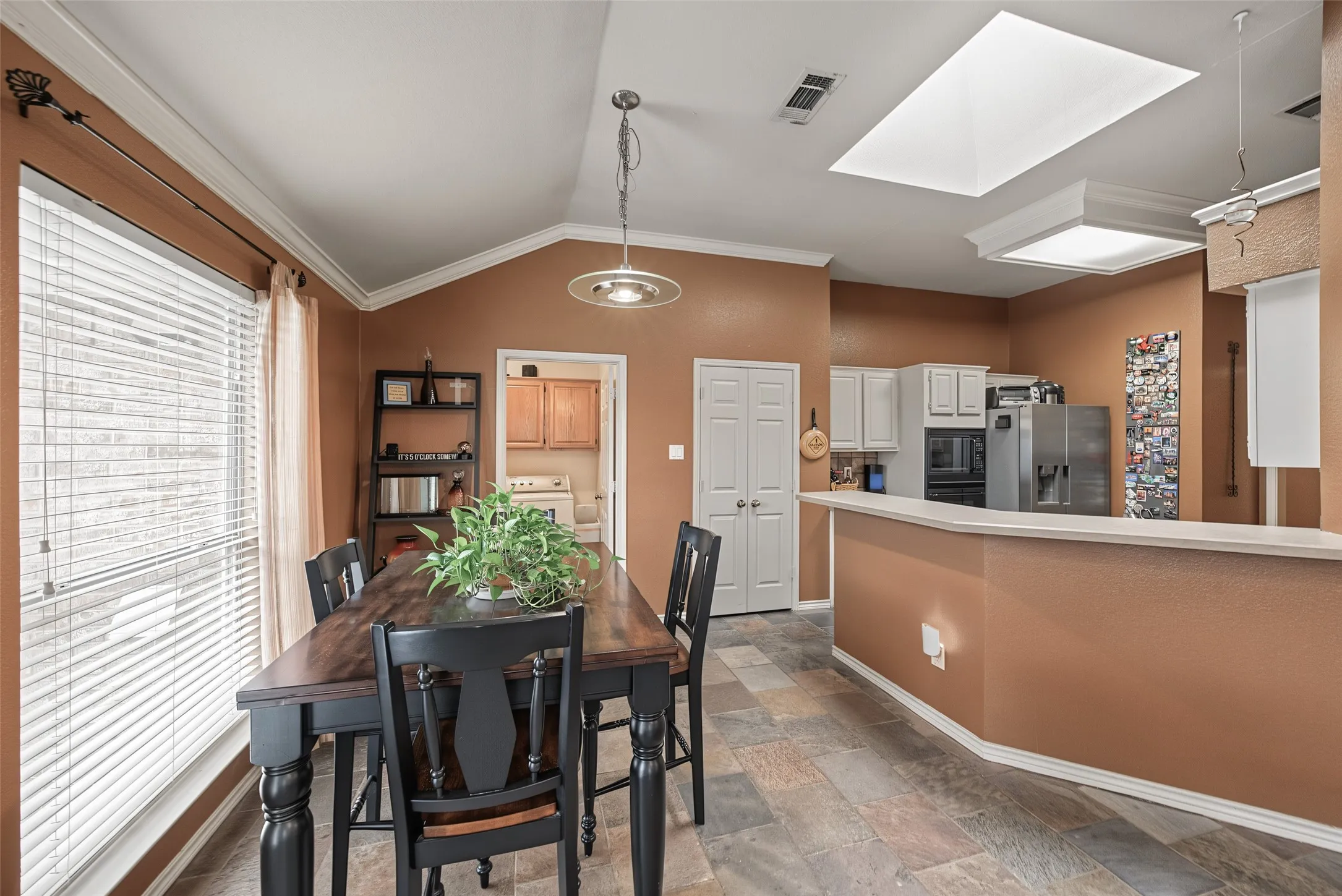 Vaulted ceiling with skylight, crown molding, tile flooring, and integrated kitchen bar with countertop