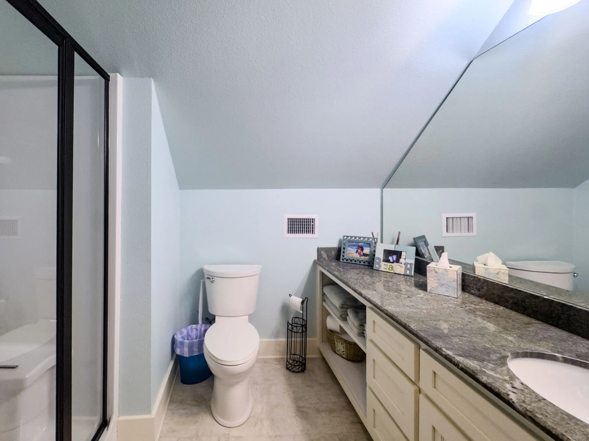 Vanity with a built-in basin and stone countertop, extensive wall mirror, built-in cabinetry, and a shower with a black-framed glass enclosure