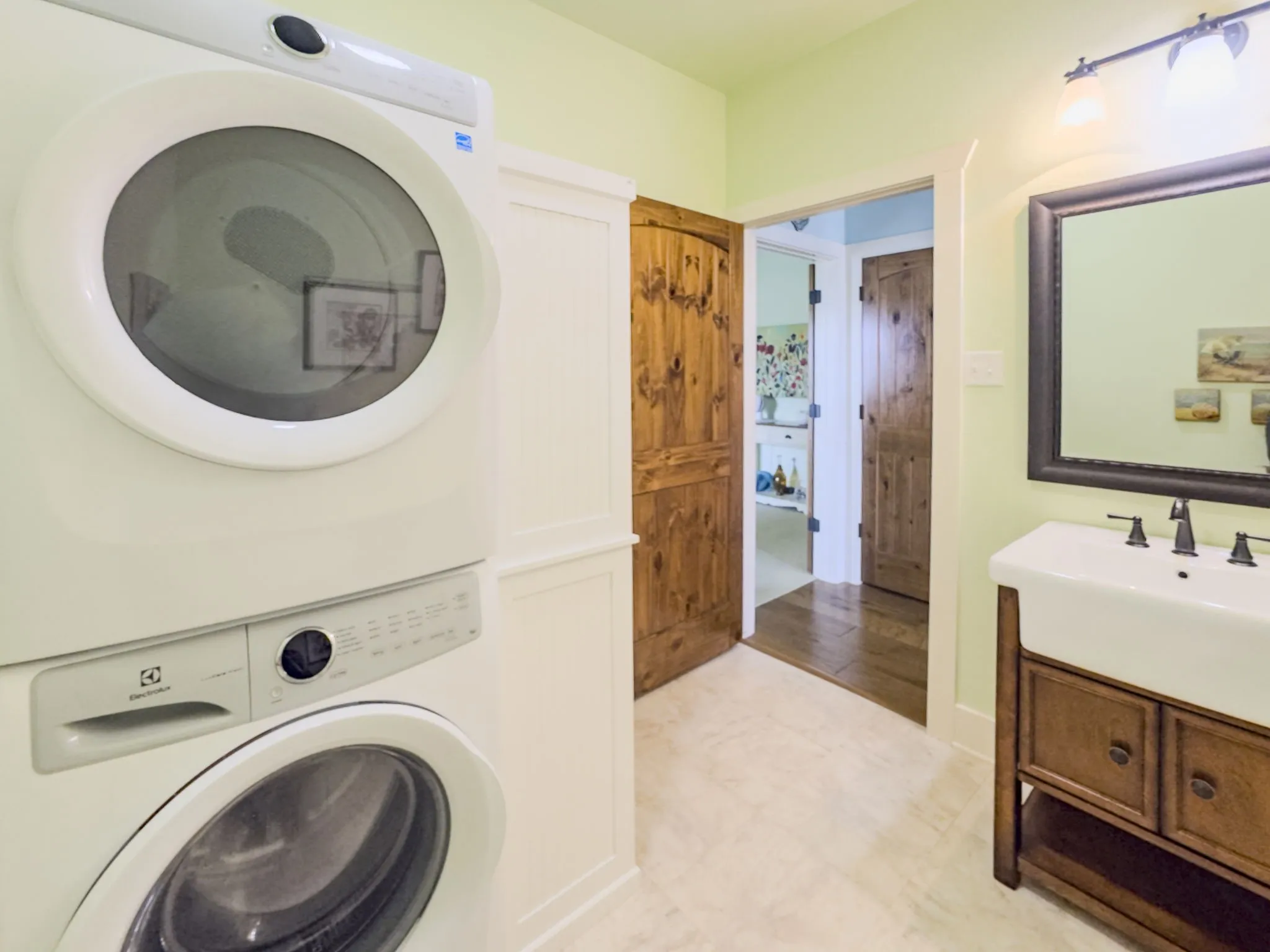 White stacked washer and dryer unit, white beadboard paneling, wood-finish doors, wood-finish vanity with an integrated sink, and an ornamental framed mirror