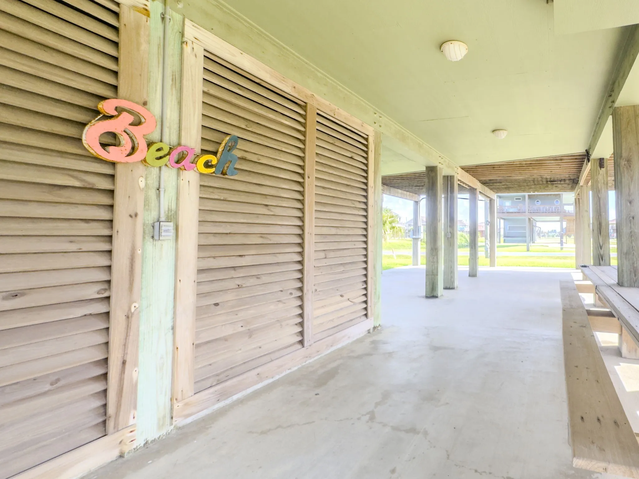 Covered outdoor space featuring a concrete slab, wood support columns, and shuttered wall panels