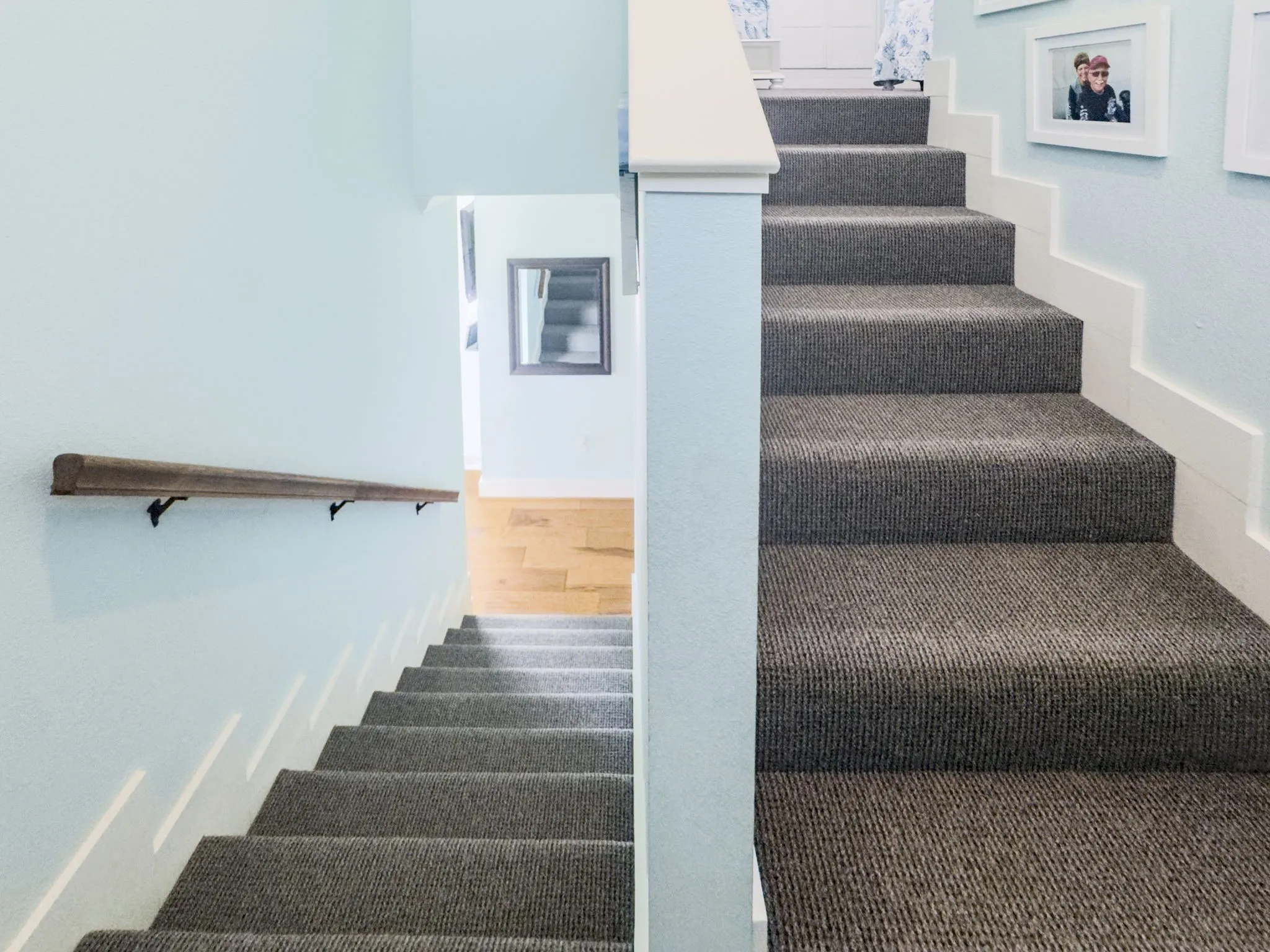 Carpeted staircase featuring a wood handrail and painted risers