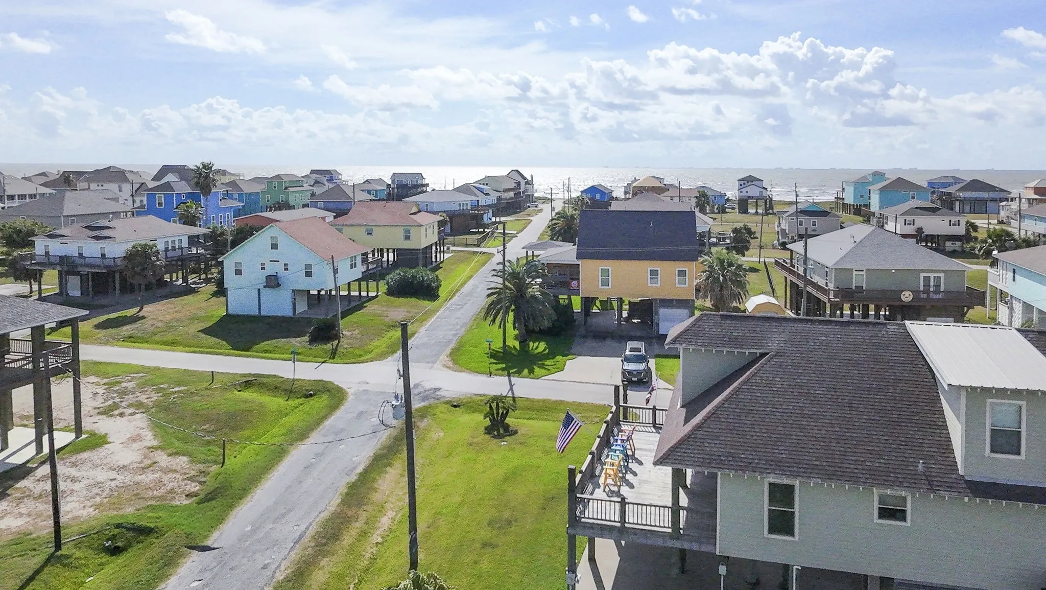Coastal neighborhood featuring elevated homes, paved streets, and a distant water backdrop