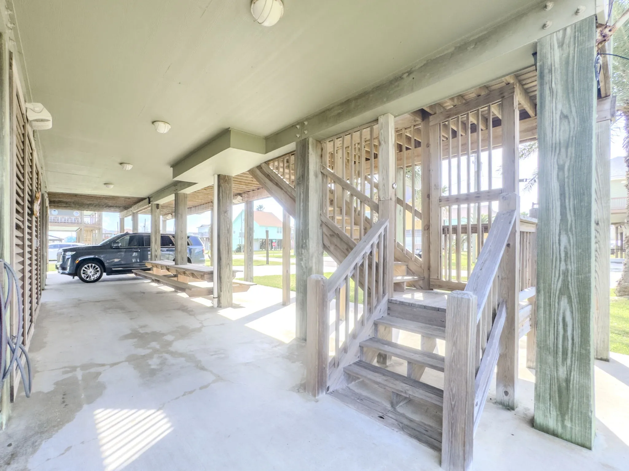 Covered parking area with concrete flooring, wood posts, and built-in wood stairs