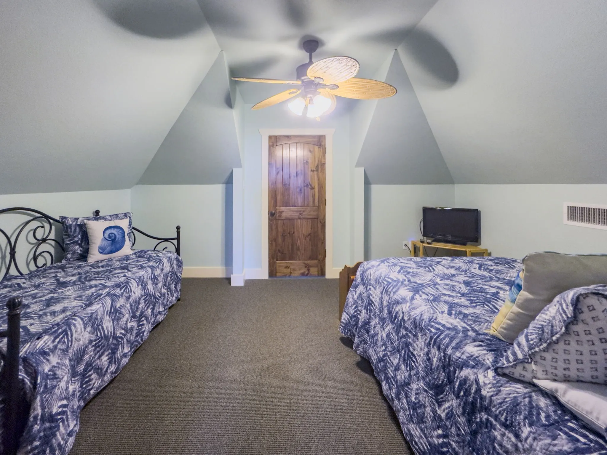 Vaulted ceiling room with a wood-finish door, ceiling fan, and carpeted flooring