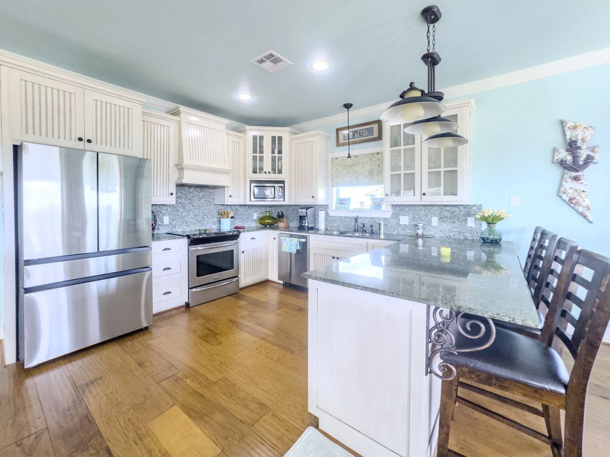 Stainless steel appliances, wood-finish flooring, white cabinetry with glass inserts, peninsula island with a stone countertop, and mosaic tile backsplash