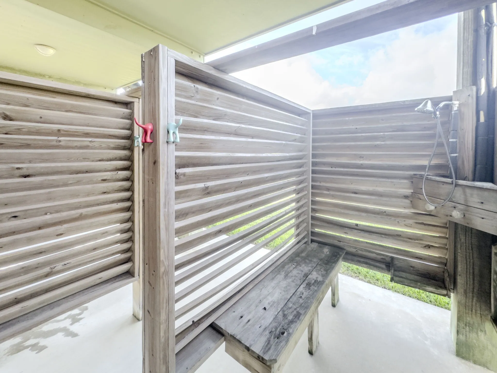 Outdoor shower featuring slatted wood walls, a built-in wood bench, and a mounted showerhead