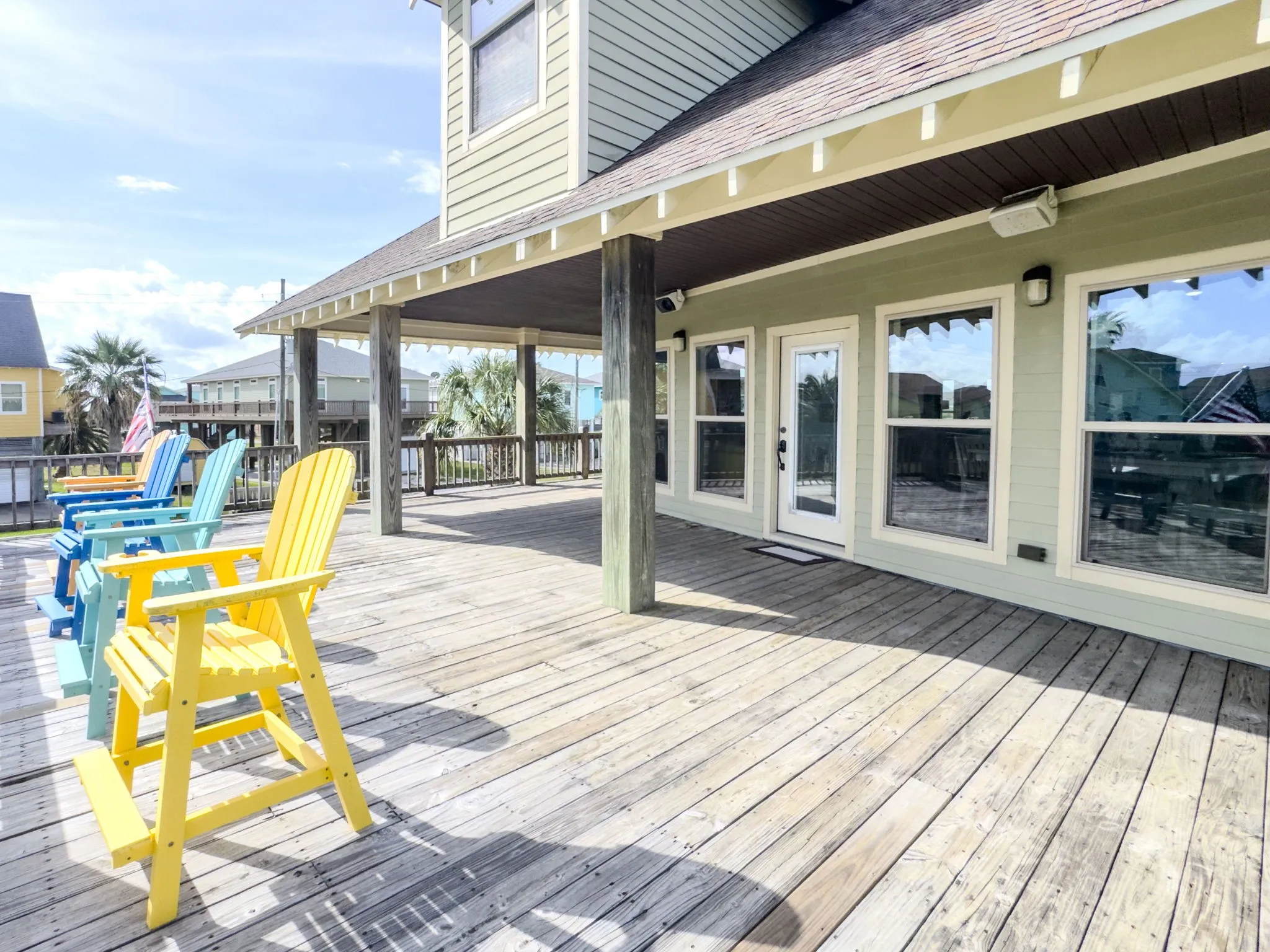 Expansive outdoor deck with wood plank flooring, covered patio area, white-framed windows, and a glass-paneled exterior door