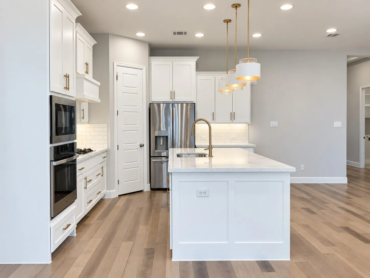 Kitchen featuring light wood-finish flooring, white cabinetry with gold-tone hardware, a center island with a sink and pendant lighting, stainless steel appliances