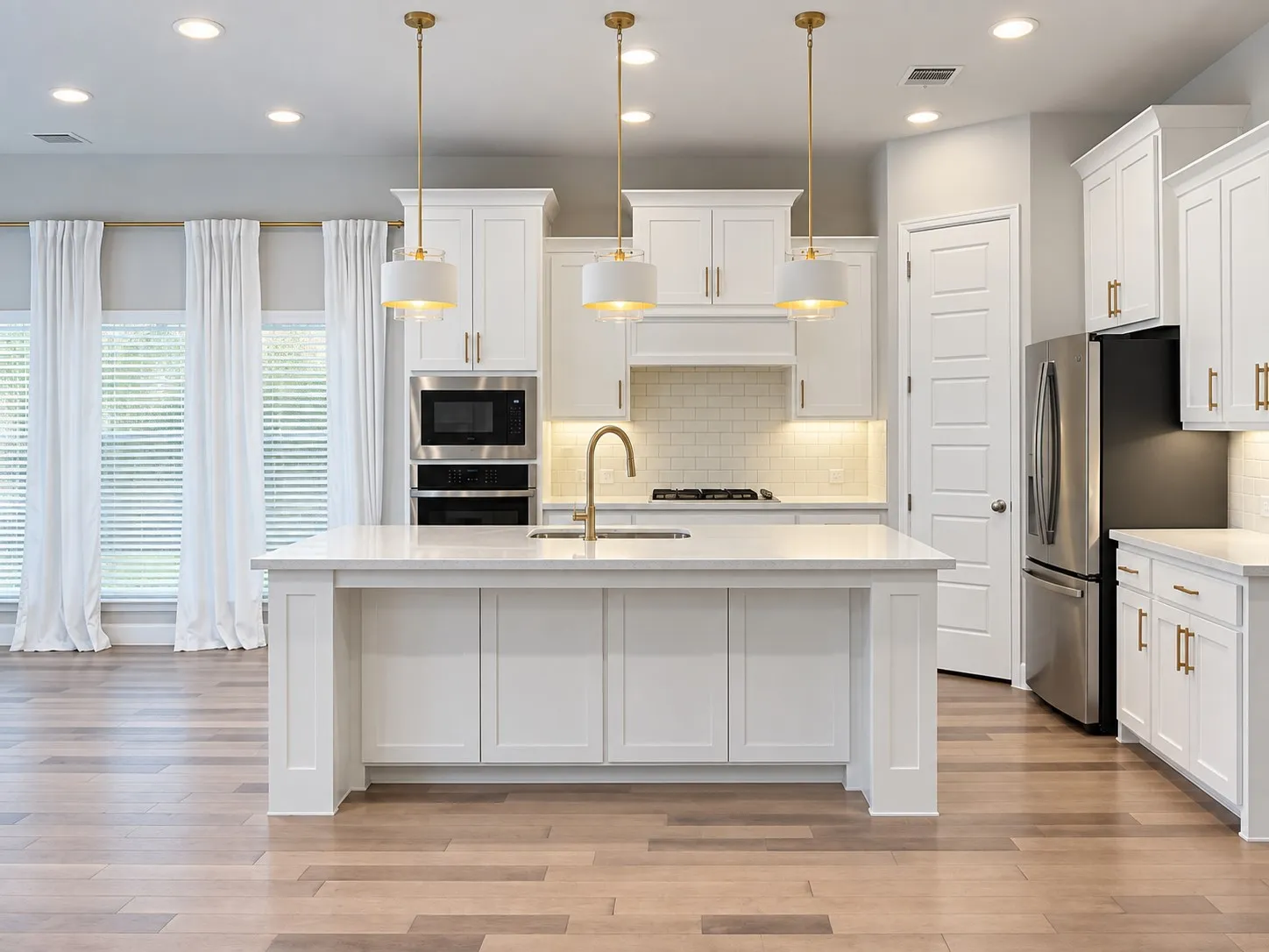 Kitchen featuring a large center island, white cabinetry with gold-tone hardware, stainless steel appliances, and wood-finish flooring