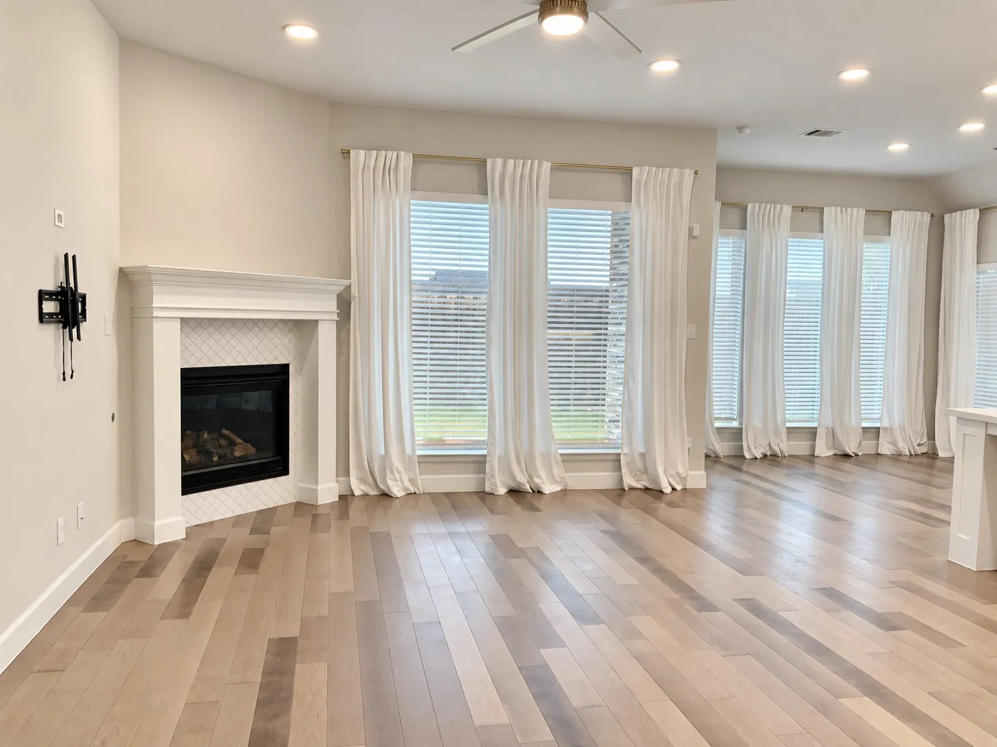 Wood-finish flooring, recessed lighting, and a corner fireplace with a tiled surround