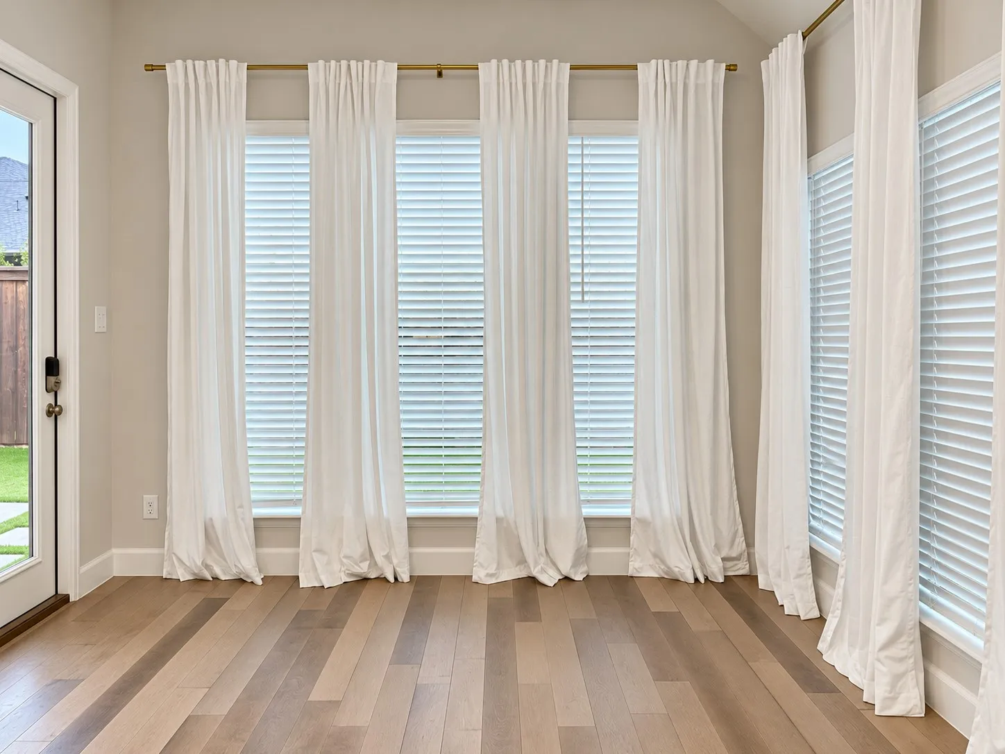 Wood-finish flooring with a light tone, multiple windows featuring privacy blinds,
