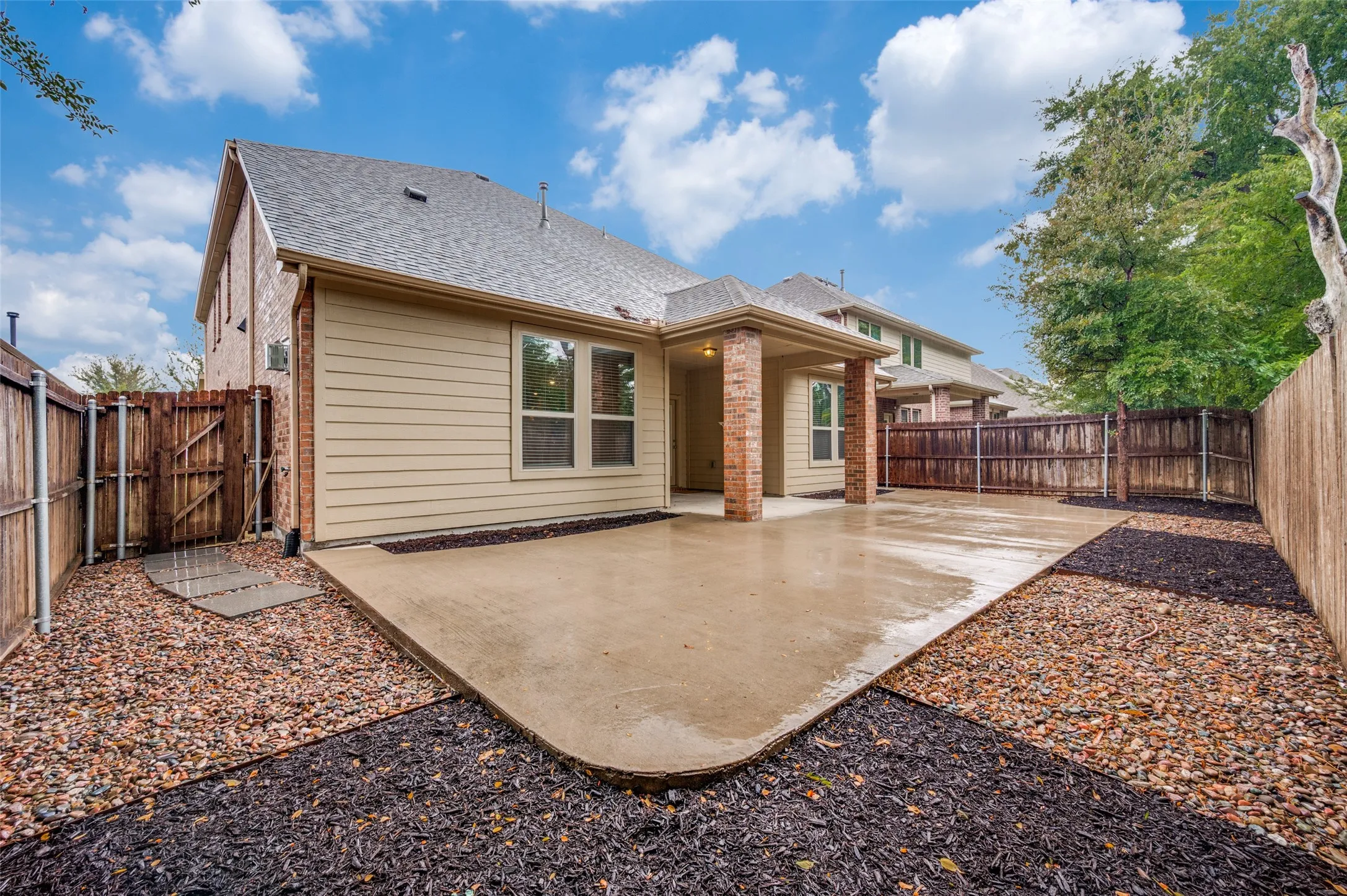 Expansive concrete patio with brick support columns, vinyl siding, and wood fencing