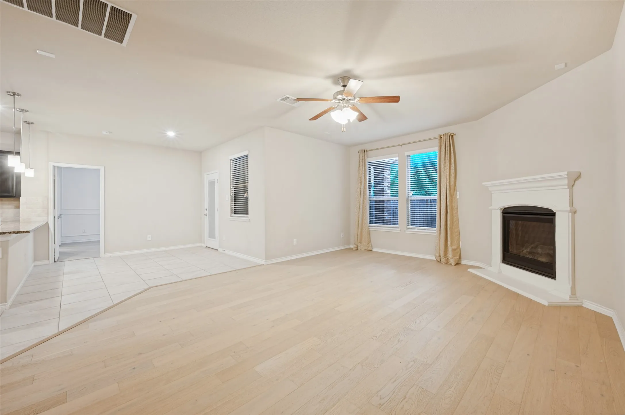 Living area featuring wood-finish flooring, a white mantel fireplace, and a ceiling fan
