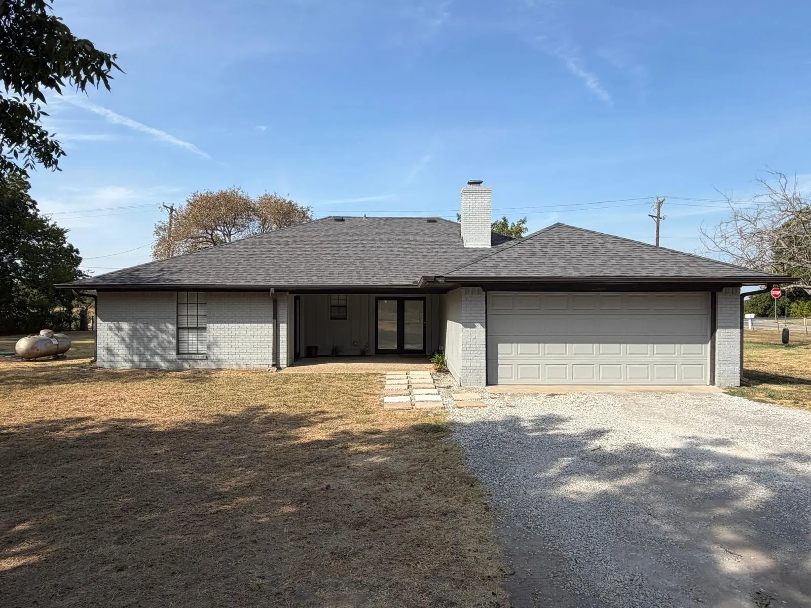 Grey brick exterior with a dark shingled roof, attached two-car garage, and a covered entry