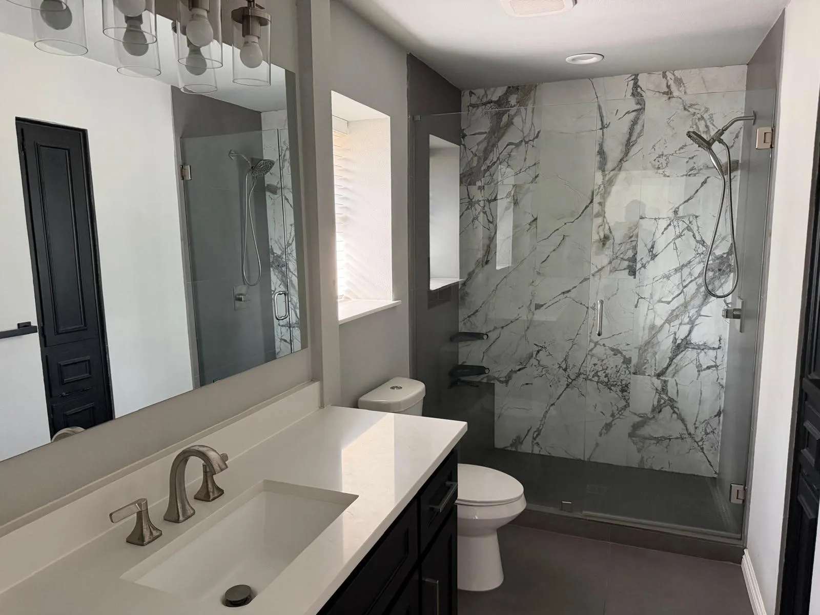 Glass-enclosed shower with white and grey veined wall tile and built-in shelving