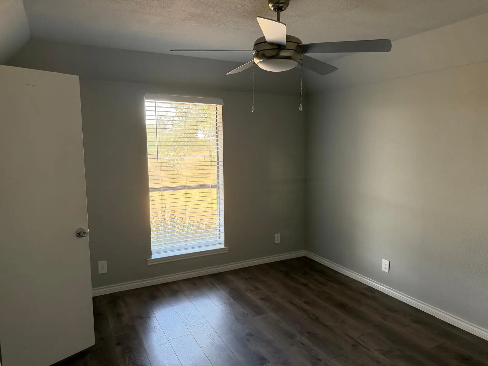 Wood-finish flooring, neutral wall tones, window with horizontal blinds, and a ceiling fan with integrated lighting
