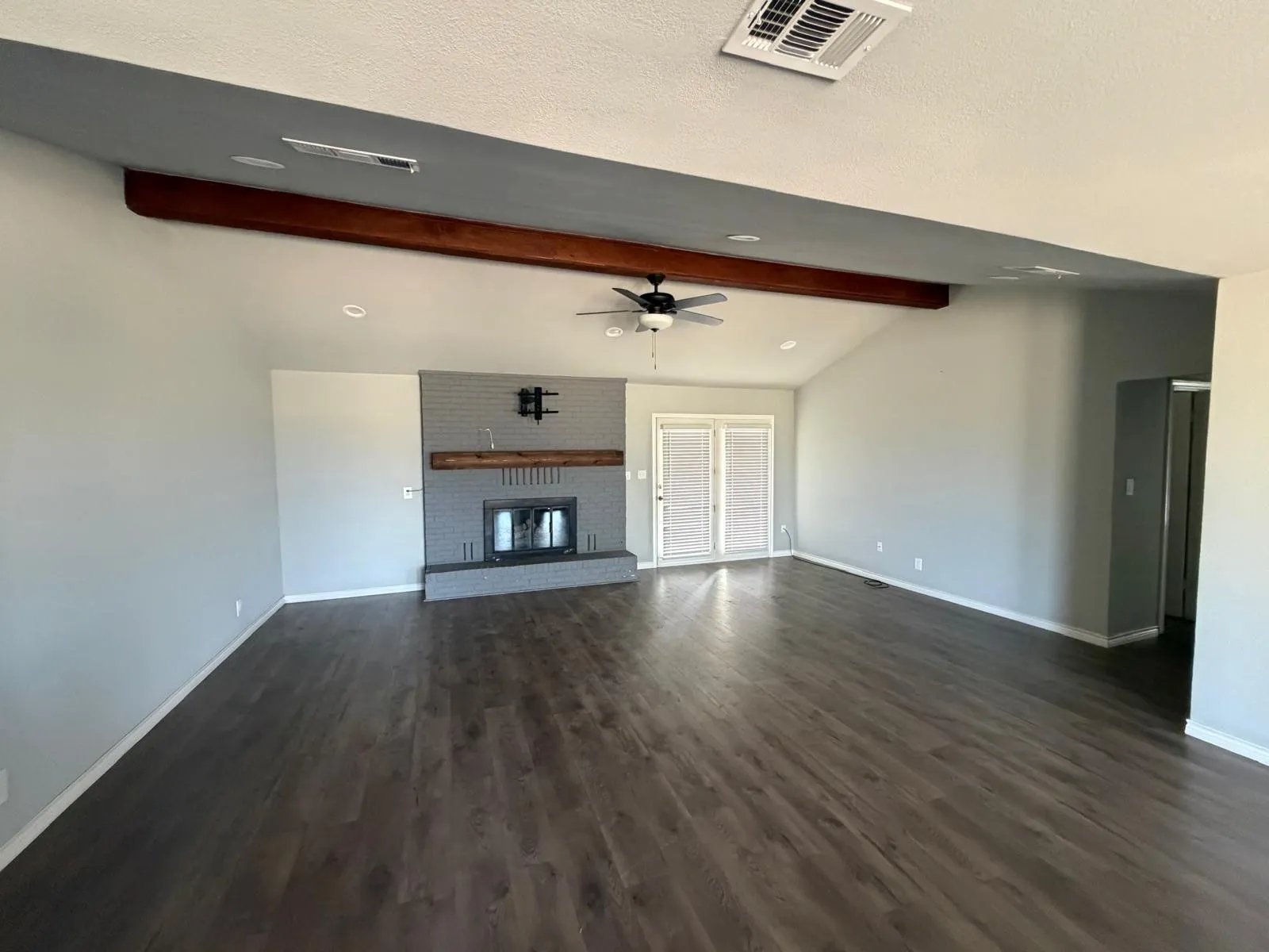 Vaulted ceiling with an exposed wood beam, wood-finish flooring, brick fireplace with a wood mantel, and double French doors