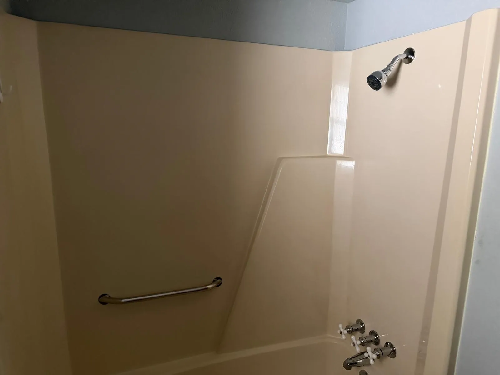 Integrated tub and shower unit with a chrome shower head, chrome faucet, and a wall-mounted grab bar