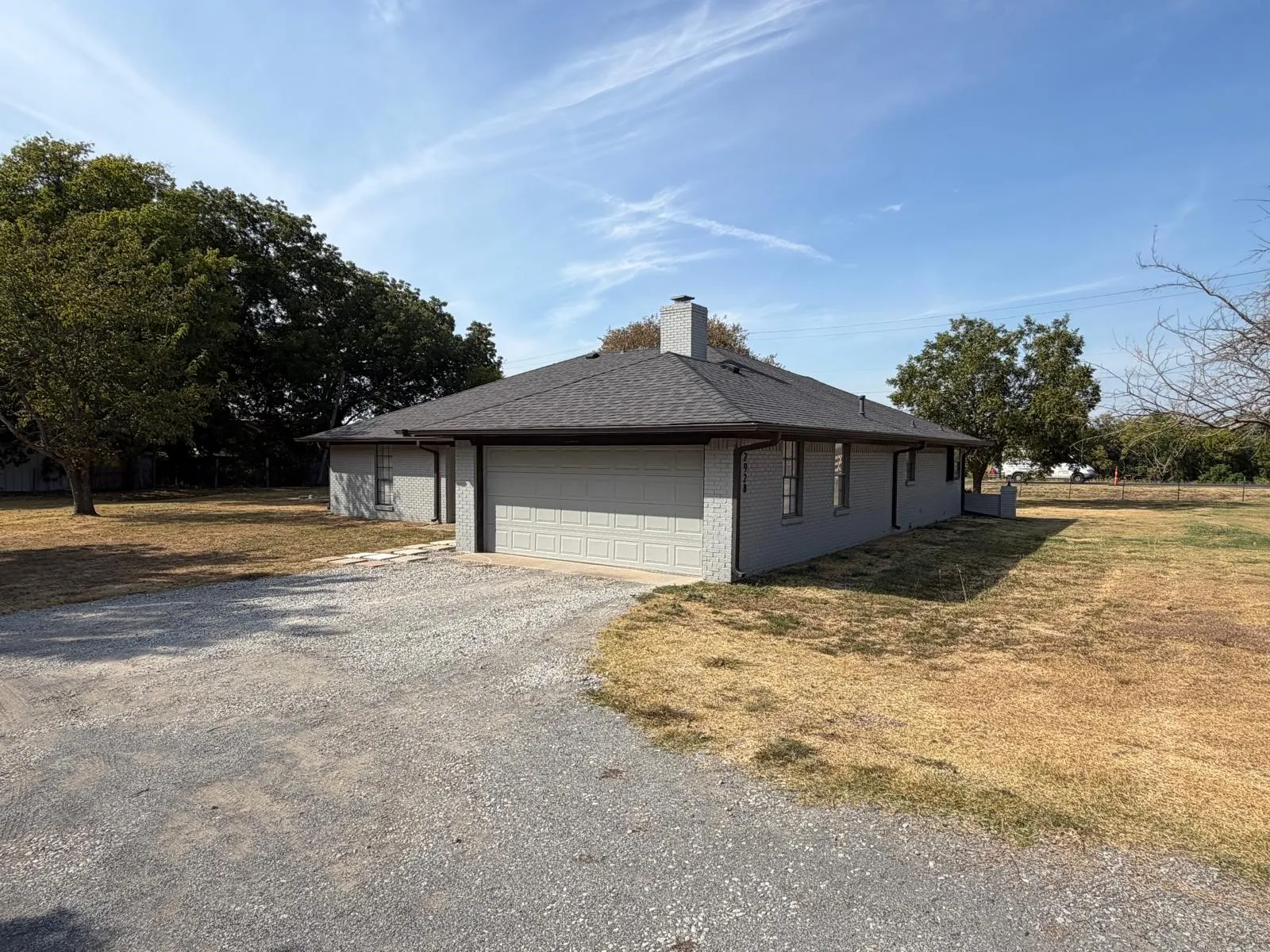 Single-story residence with a gray exterior, a dark shingle roof, and a gravel driveway