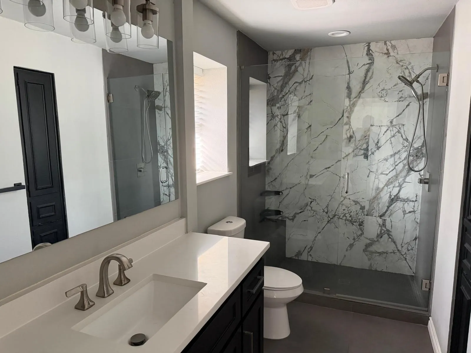 Custom glass-enclosed shower with large format marble-look tile, fixed and handheld showerheads, and recessed shelving