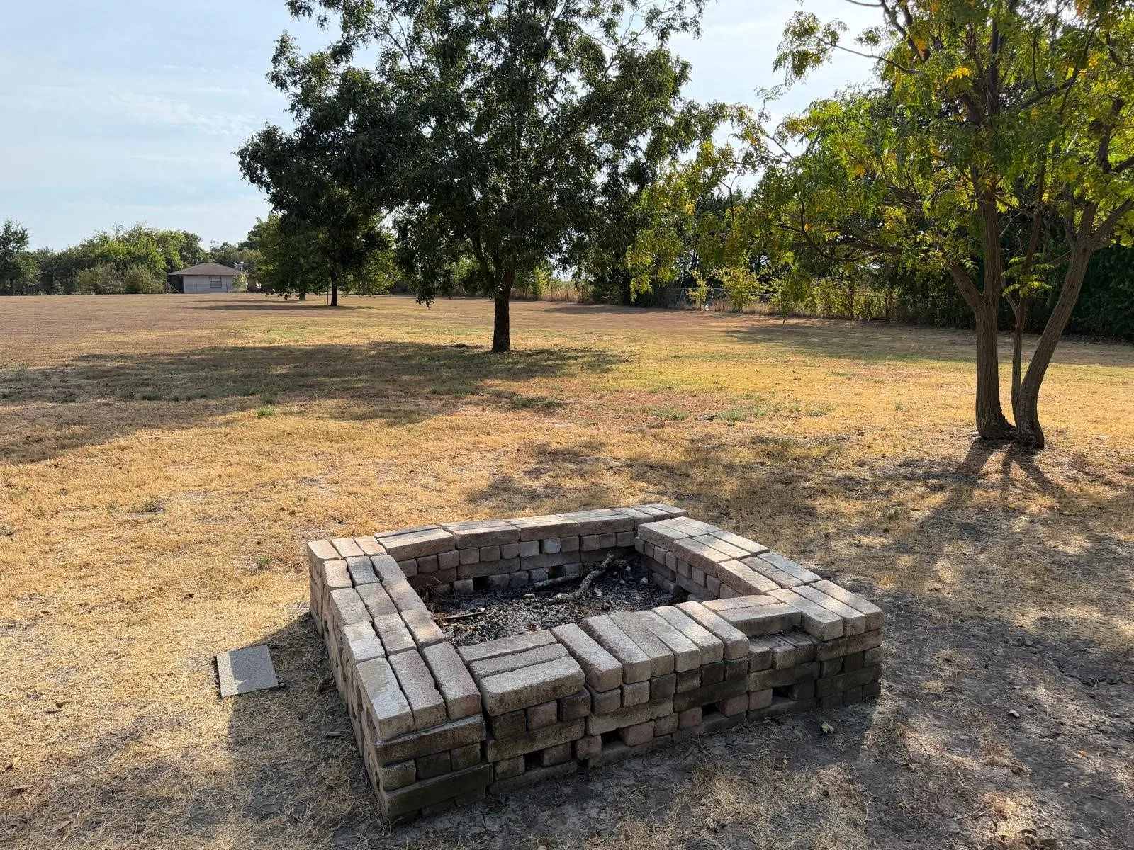 Rectangular brick fire pit feature with expansive outdoor space and mature trees