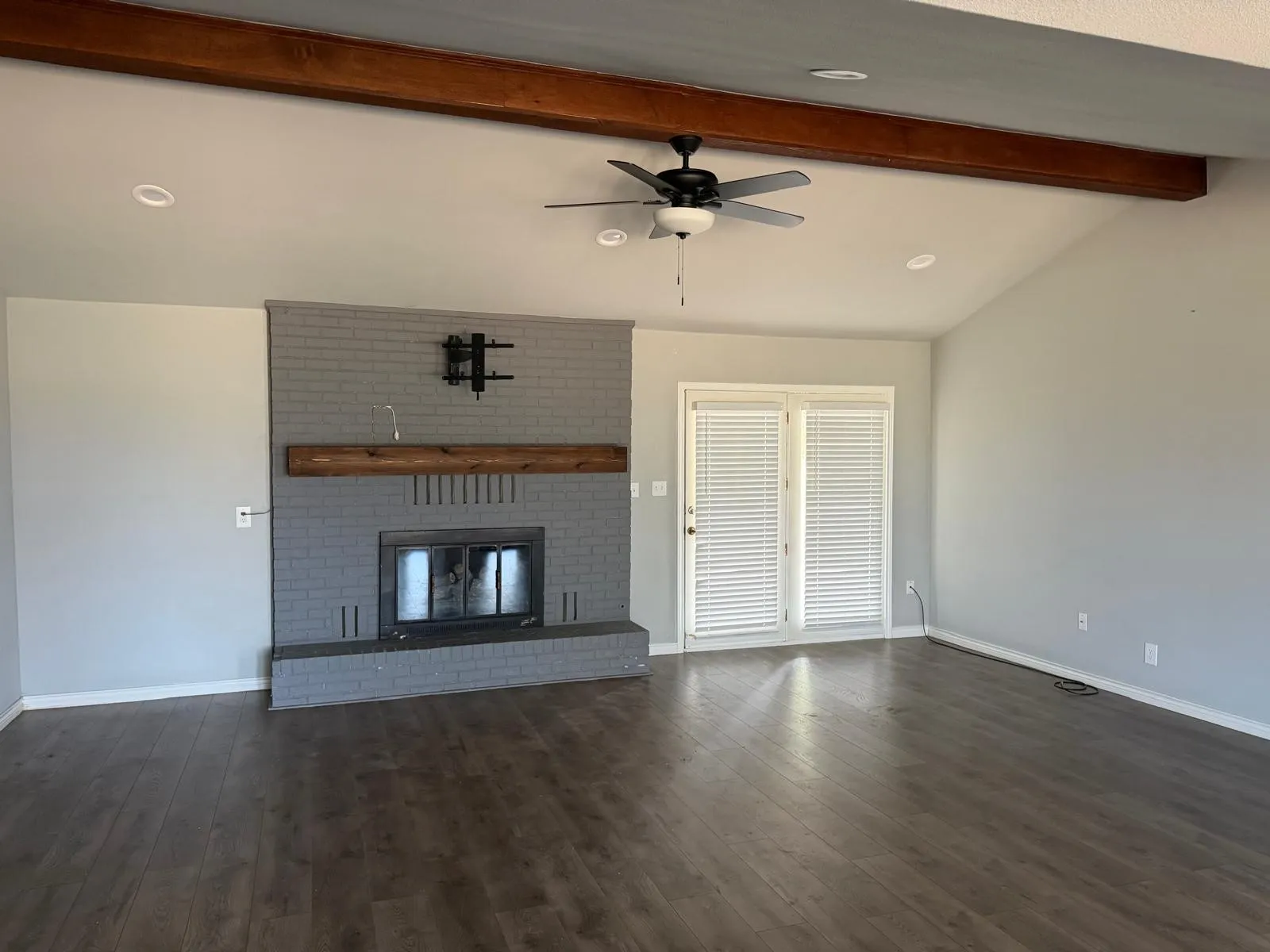 Vaulted ceiling with exposed wood-finish beam, brick fireplace with wood-finish mantel, wood-finish flooring, and double French doors
