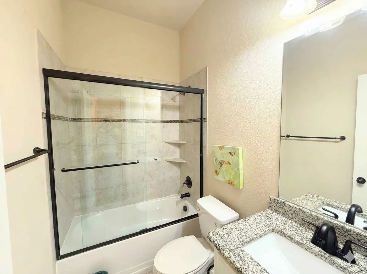 Bathroom featuring a shower-tub combination with tile surround, glass sliding doors with black hardware, and built-in shelving