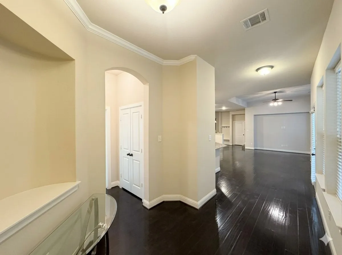 Dark wood-finish flooring throughout, white crown molding, and an arched doorway