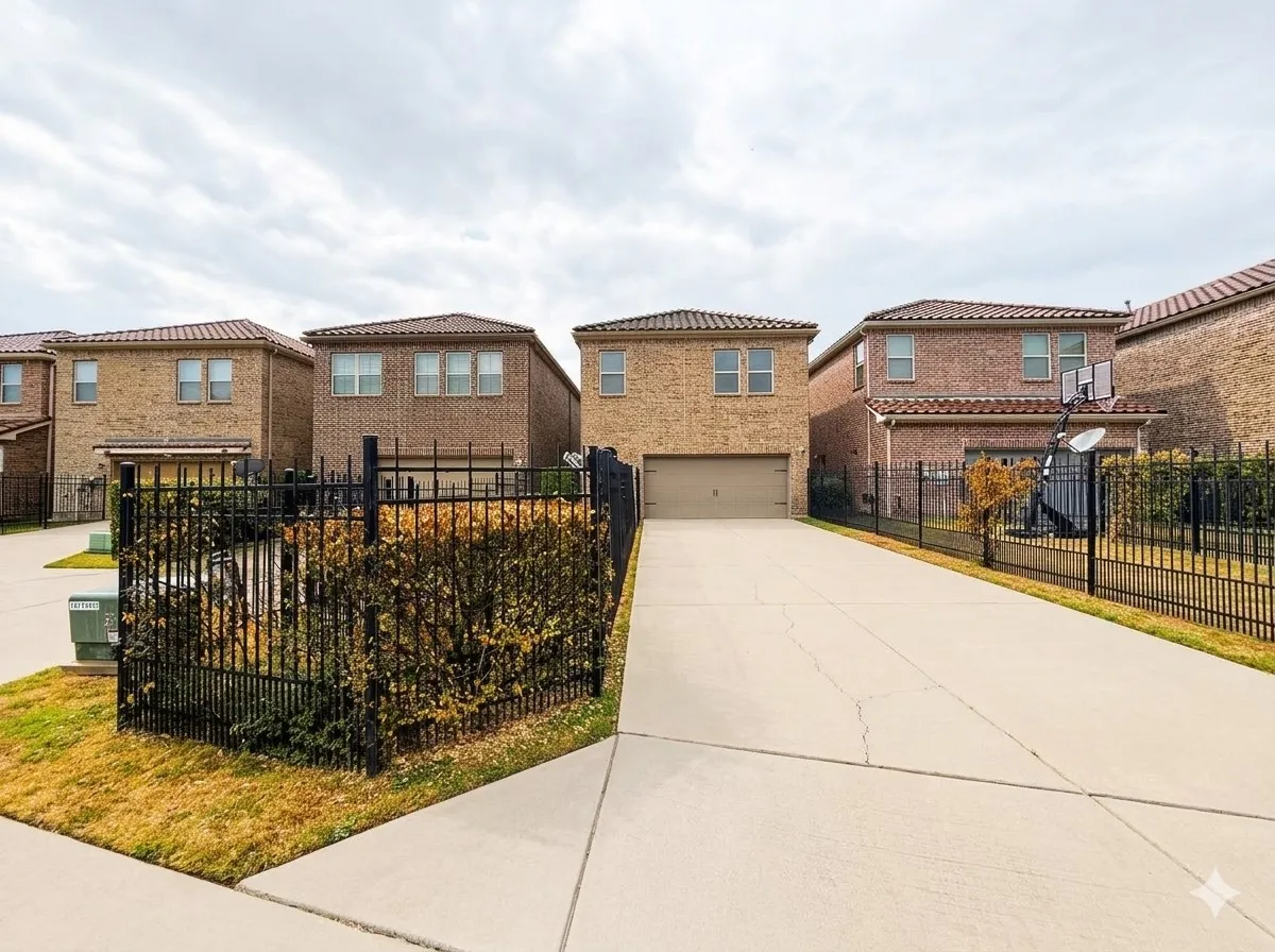 Brick exterior featuring a two-car garage, concrete driveway, and wrought iron fencing