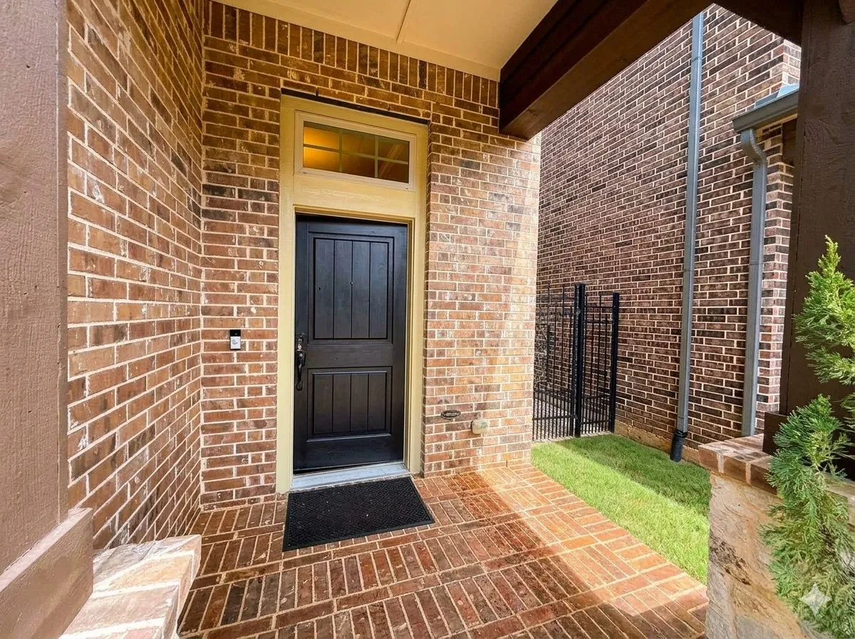 Brick exterior featuring a black paneled entry door, transom window, and a patterned brick porch