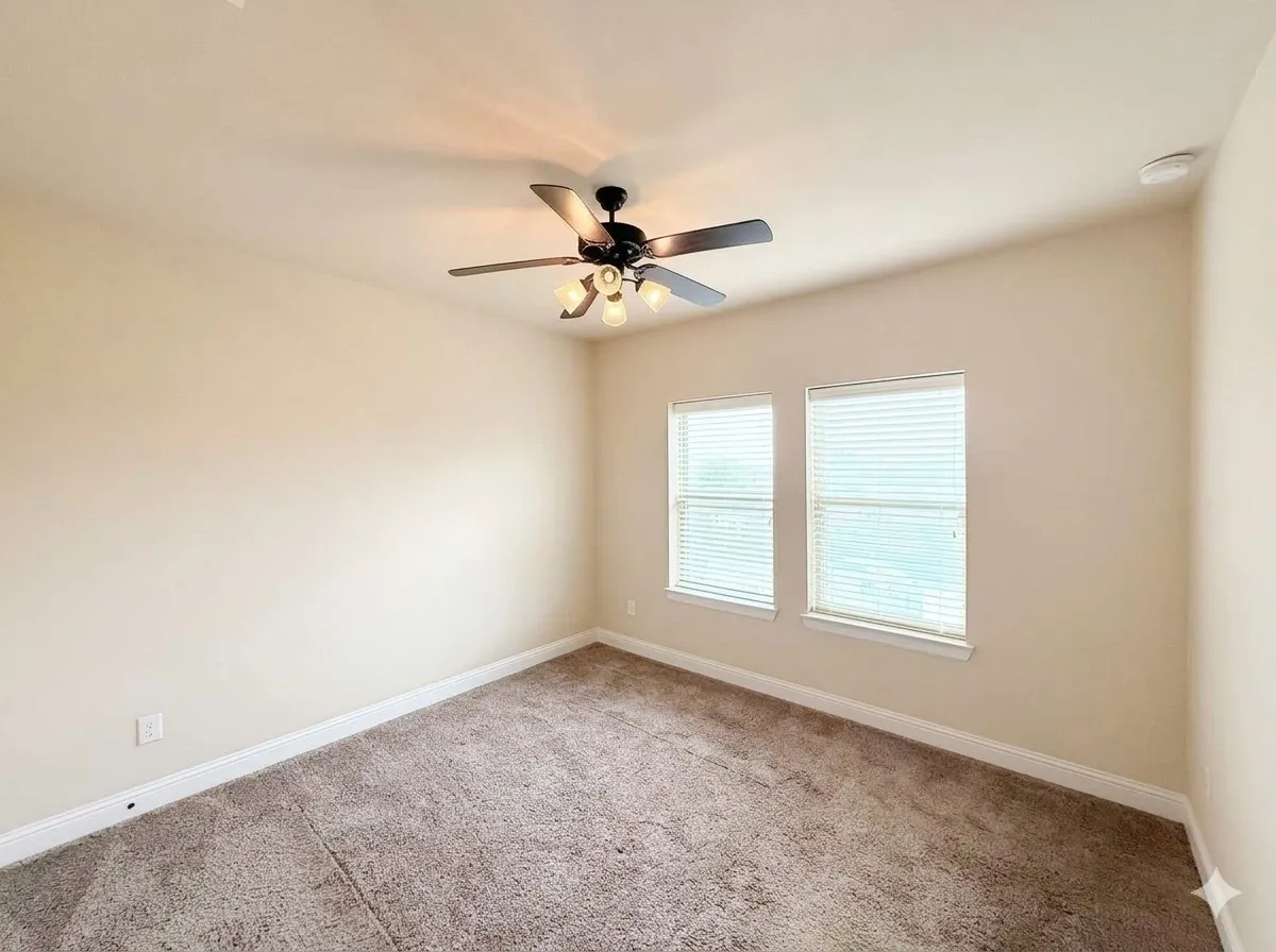 Neutral-toned walls, textured carpeting, two windows with blinds, a ceiling fan with integrated lighting, and white trim