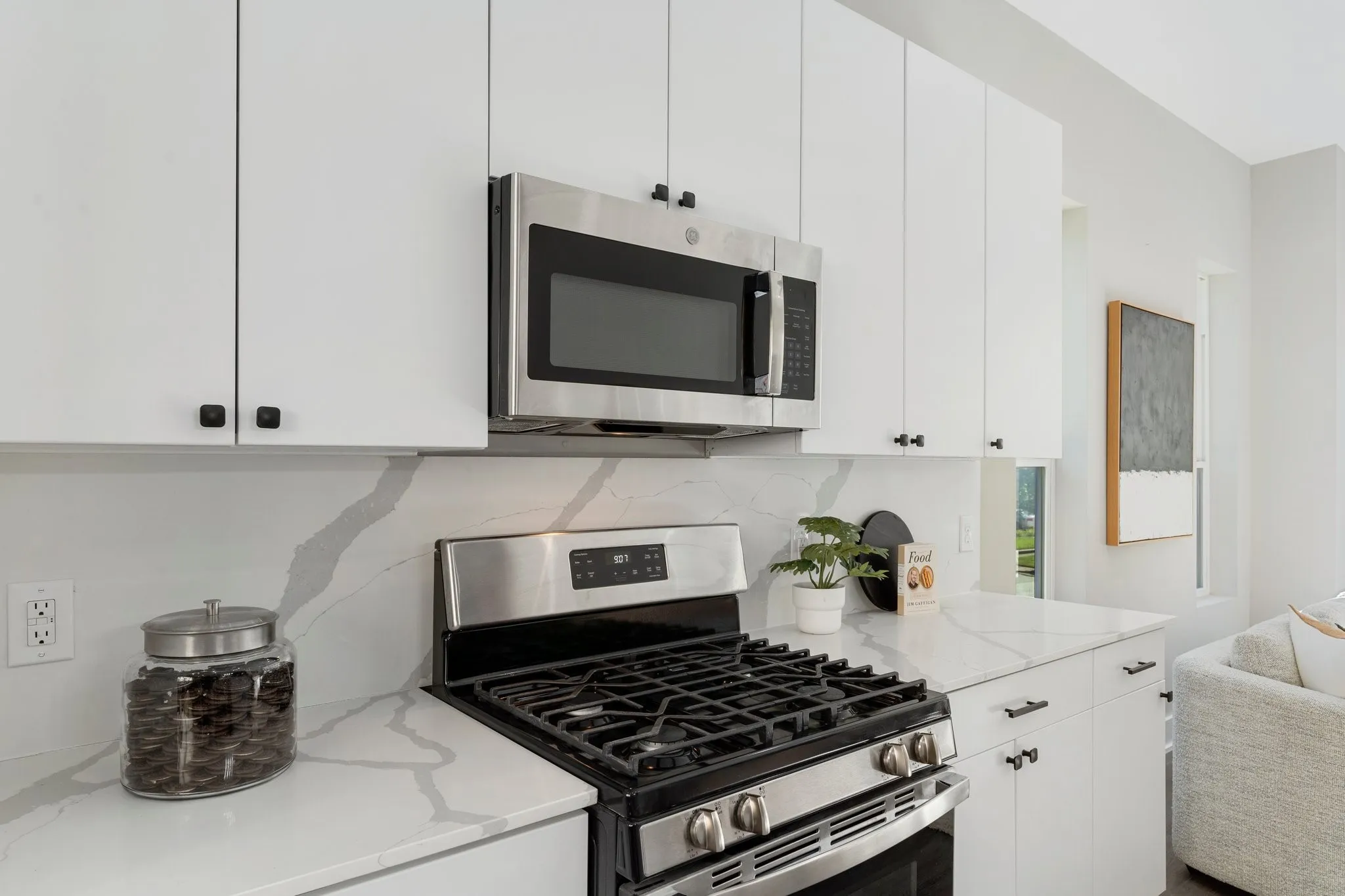 White cabinetry with matte black hardware, stainless steel range, built-in microwave, and stone countertops