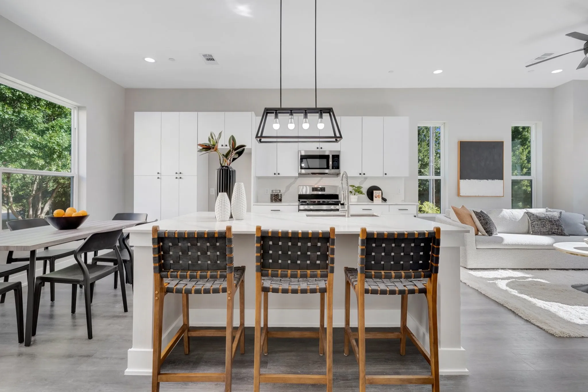 Spacious open-concept living area featuring an expansive kitchen island with a built-in sink, modern pendant lighting, and stainless steel appliances