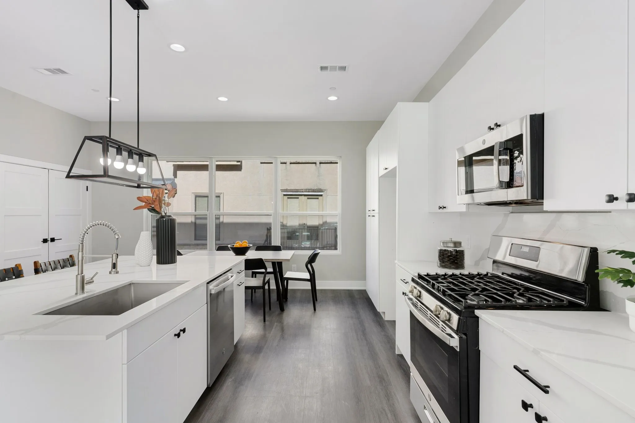 White cabinetry with stainless steel appliances, wood-finish flooring, and an island with an integrated sink