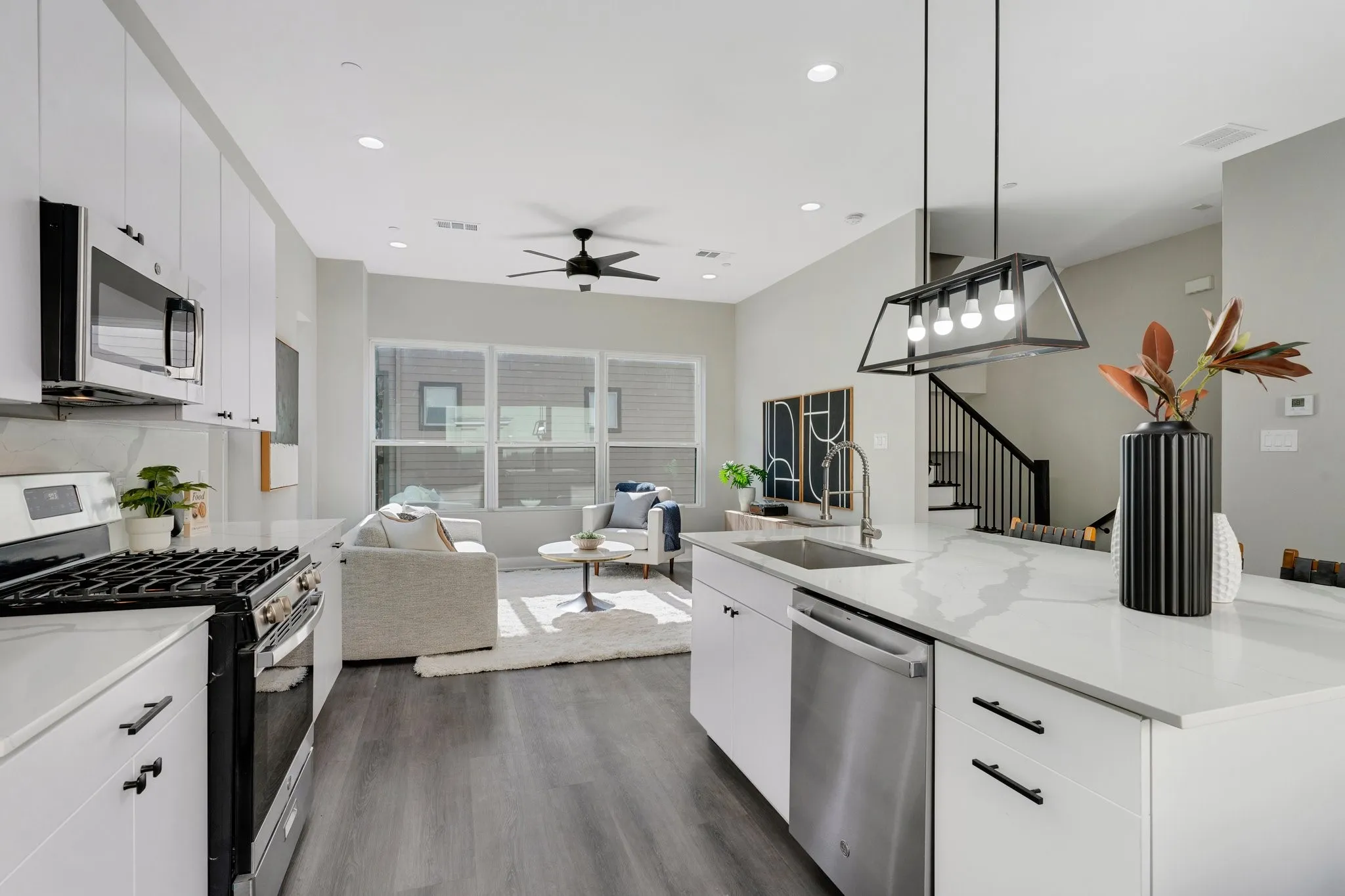 Open-concept living area with wood-finish flooring, white cabinetry, stainless steel appliances, and a kitchen island with a sink