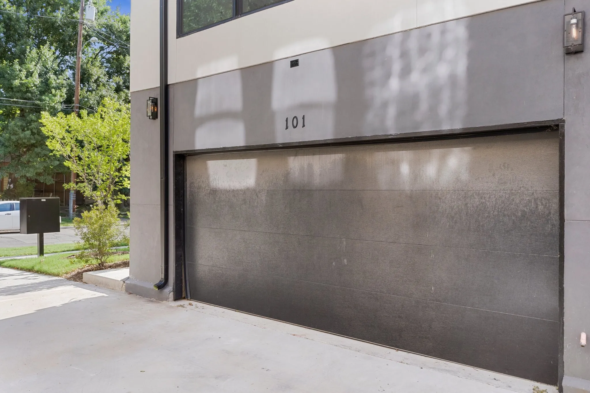 Modern exterior facade featuring a textured garage door, integrated wall sconces, and a concrete driveway