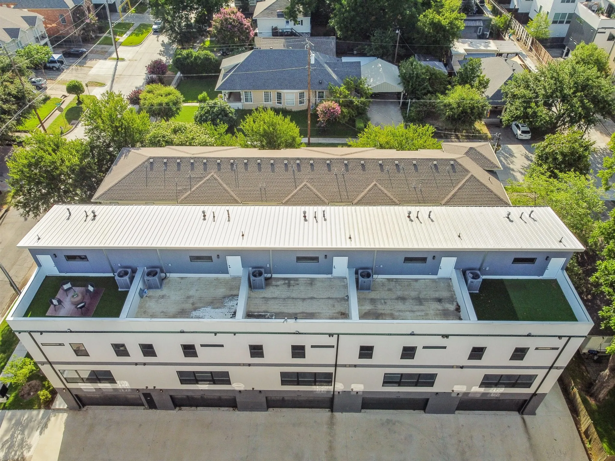 Building exterior featuring a white metal roof, multiple rooftop patios with artificial turf, and a contemporary facade with dark framed windows