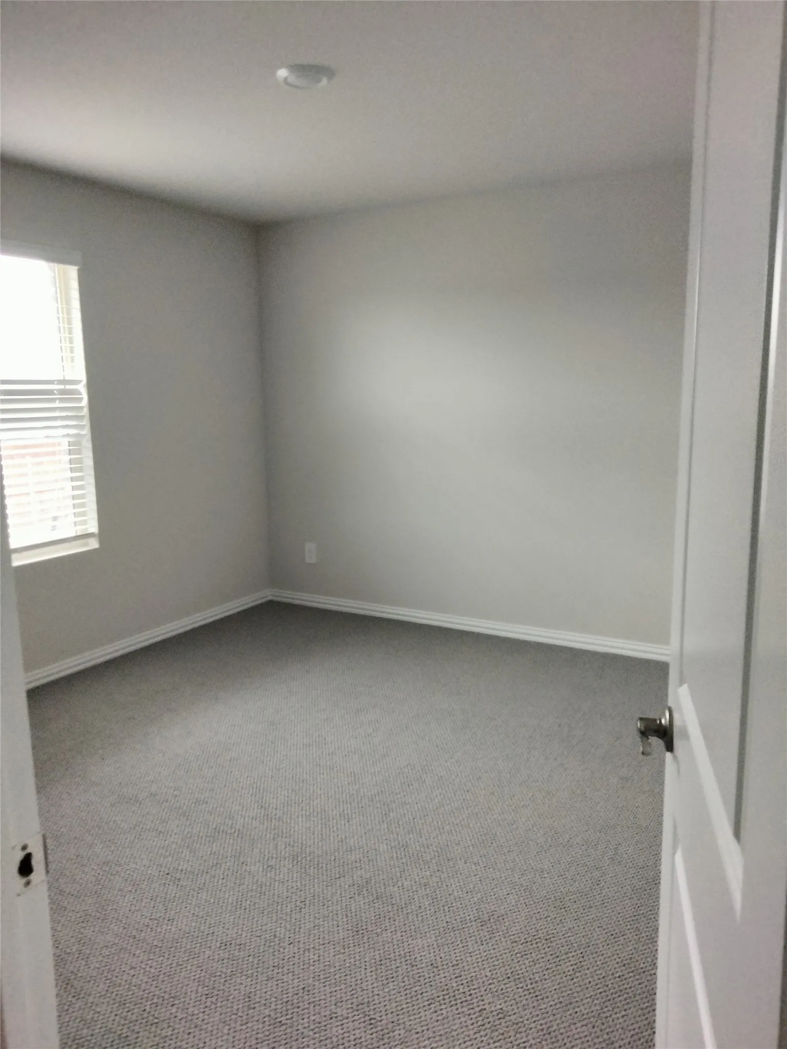 Neutral tone wall paint, grey textured carpet, white trim, recessed ceiling light, and a window with blinds