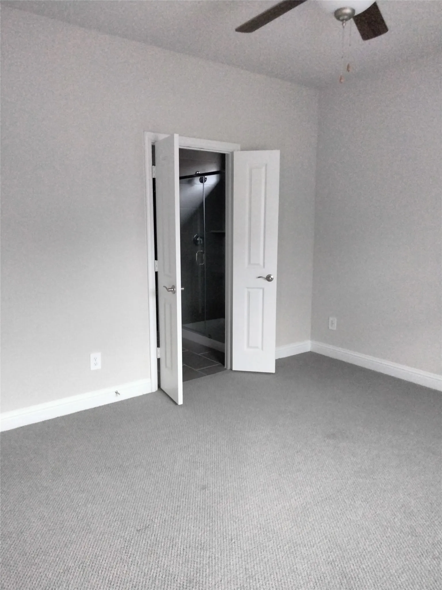 Carpeted flooring, light gray wall paint, white trim, ceiling fan, and an open doorway to a tiled shower area