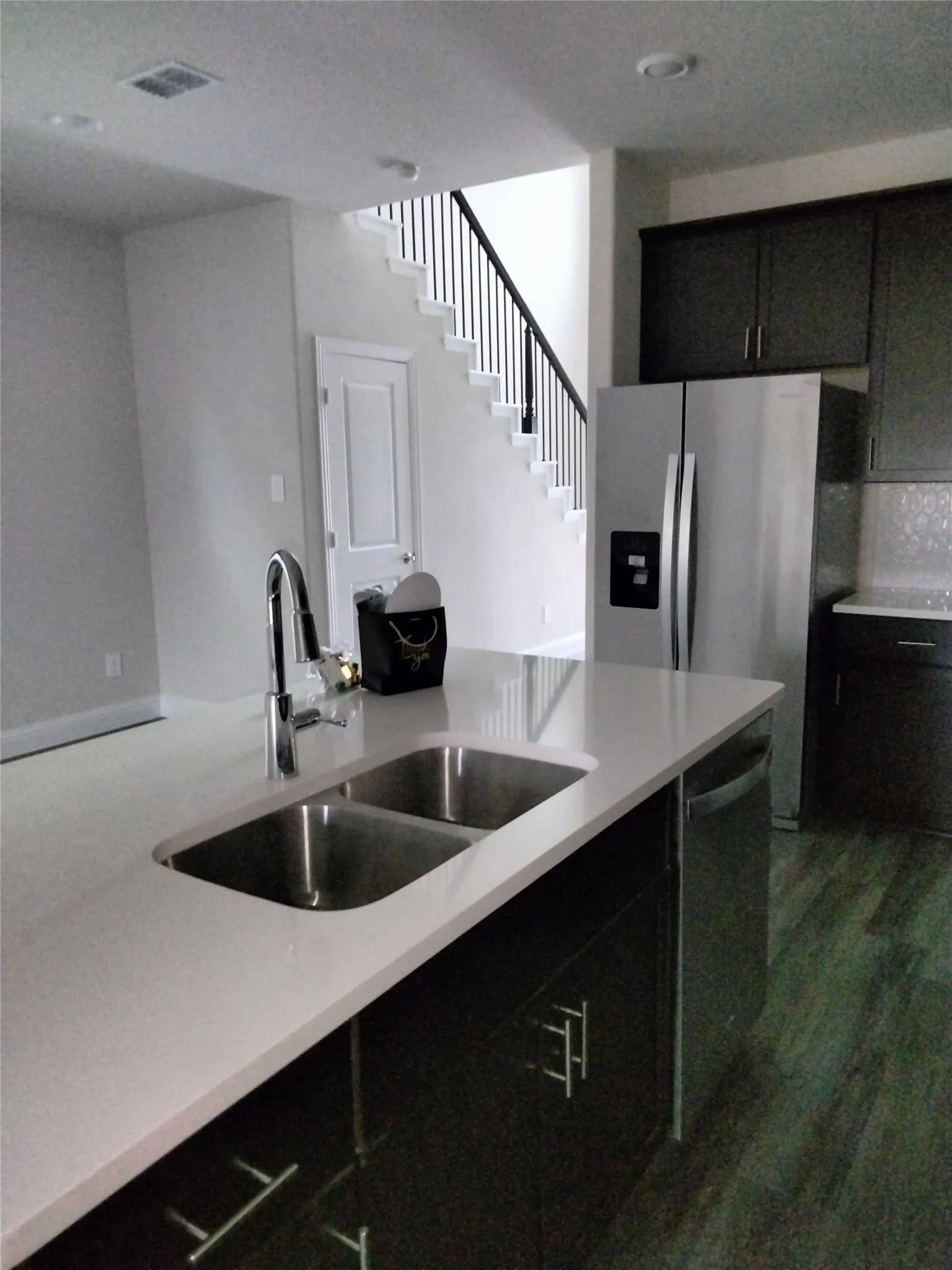 Kitchen island with an undermount double basin stainless steel sink, a pull-down faucet, light-toned countertop, and dark cabinetry