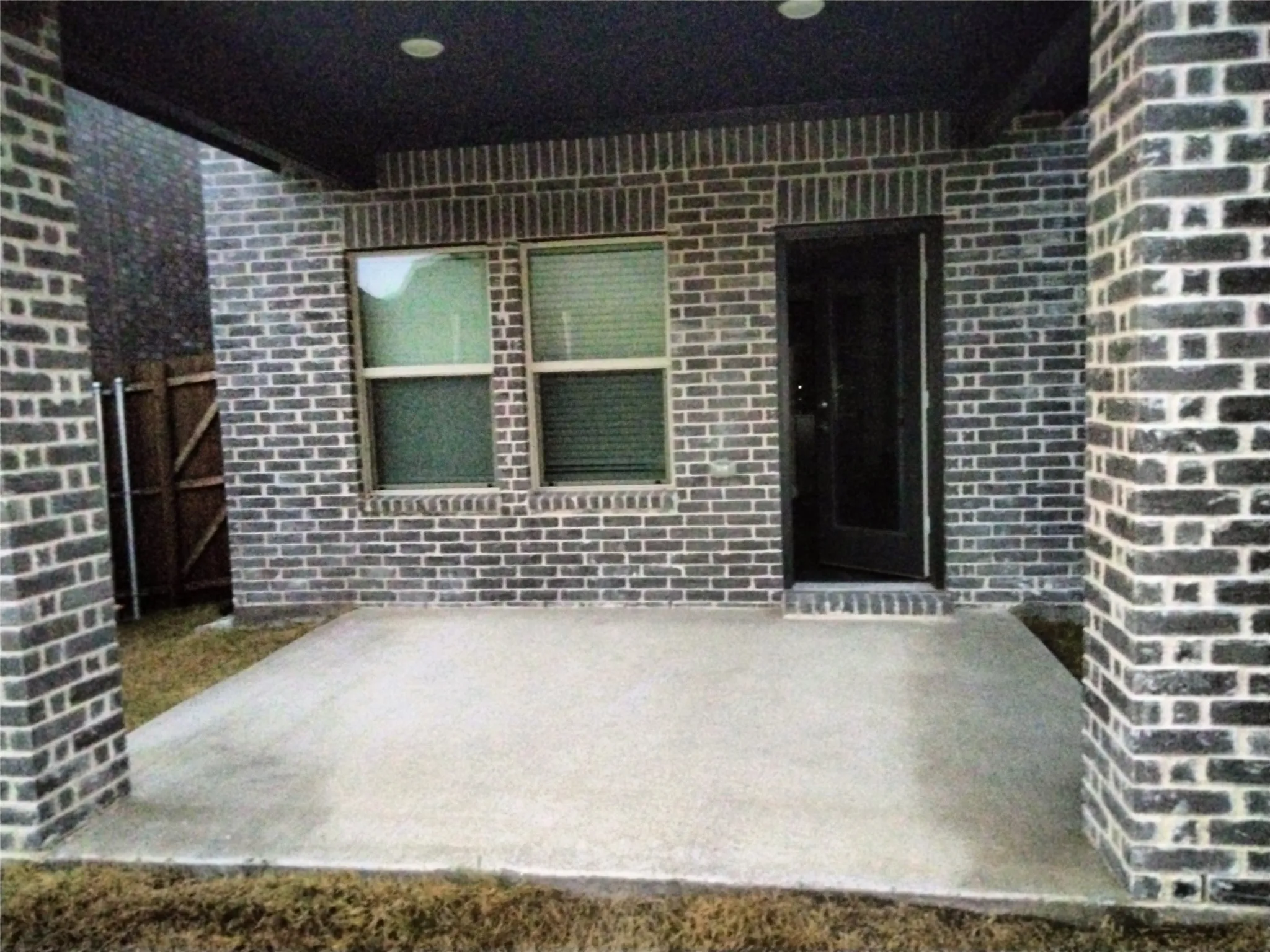 Concrete patio featuring a dark brick exterior, recessed lighting, and a dark-framed entry door