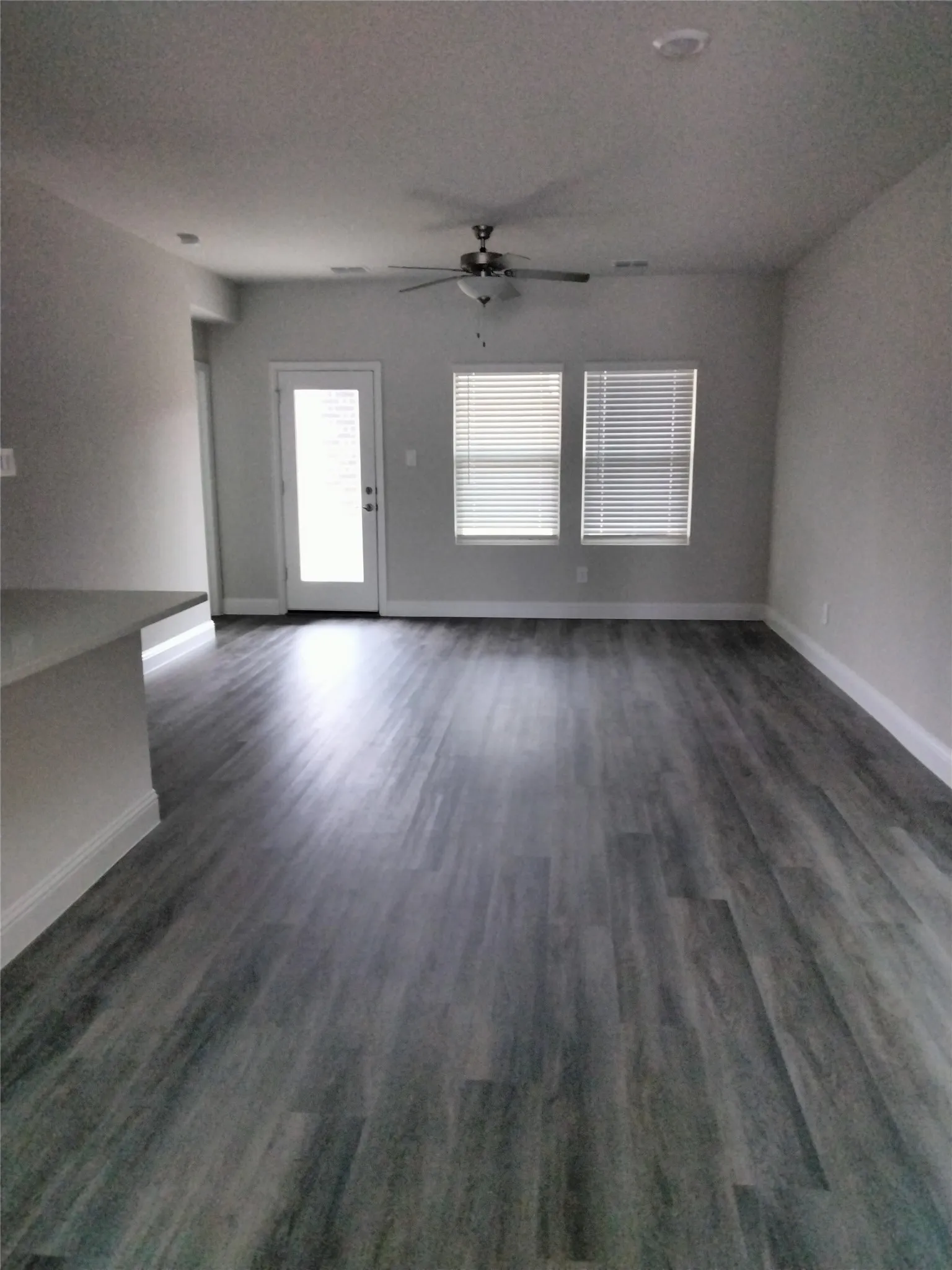 Wood-finish flooring, ceiling fan, white trim, recessed lighting, and multiple windows with blinds