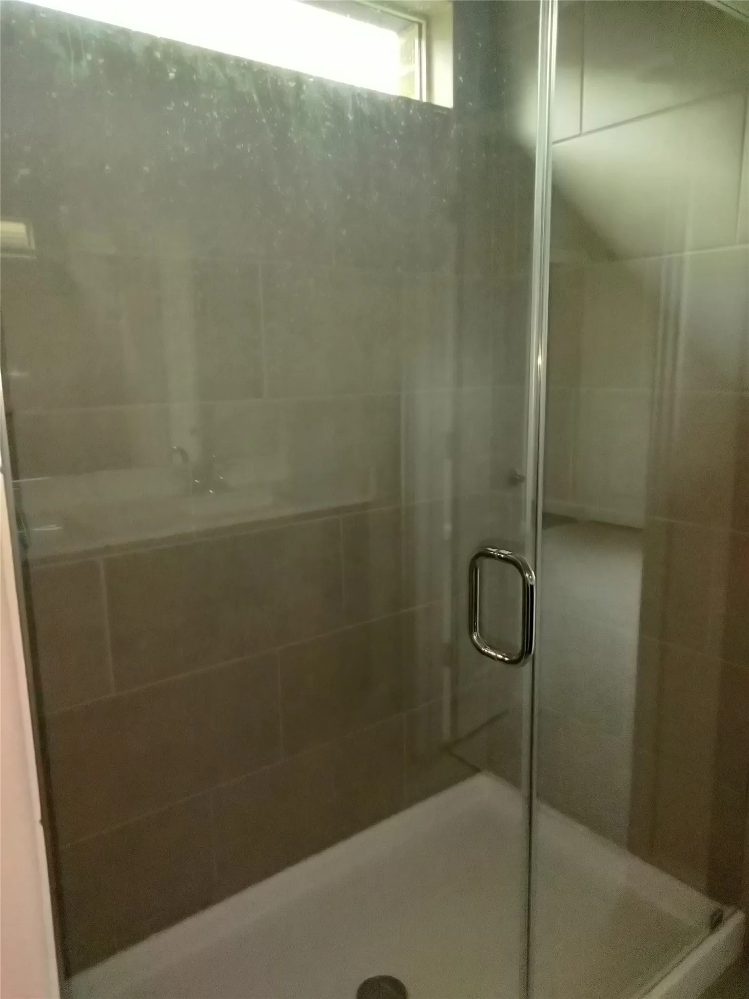 Frameless glass shower enclosure with a chrome handle, complemented by large format wall tiling and a white shower pan