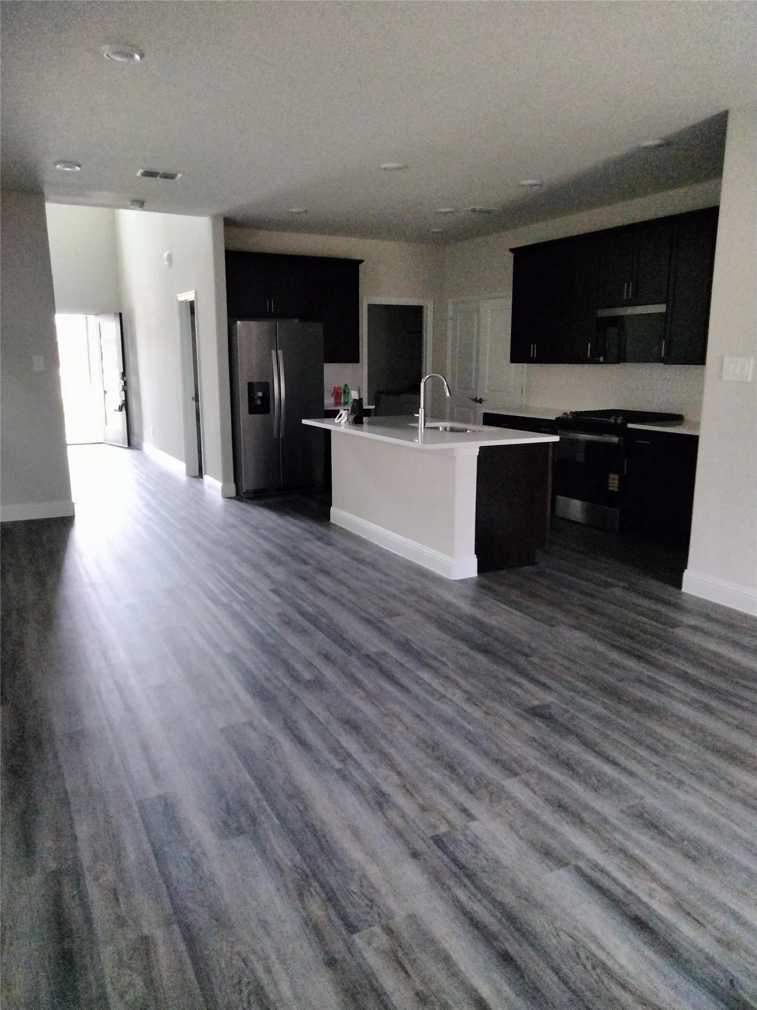 Open-concept kitchen featuring dark wood cabinetry, stainless steel appliances, a center island with sink, and light-toned countertops