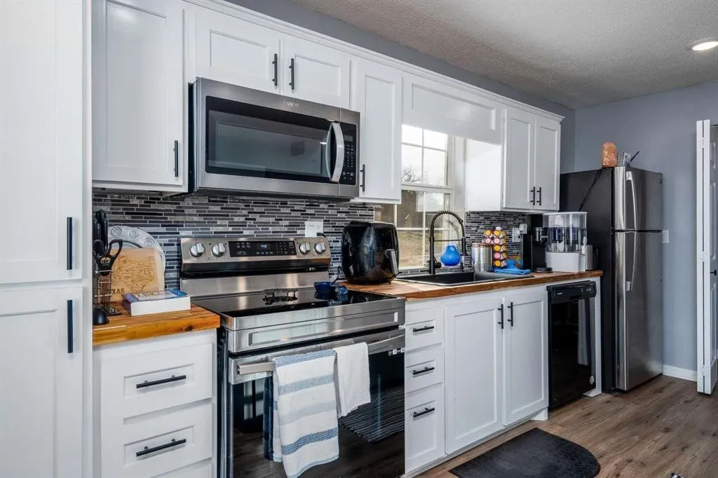 White cabinetry with matte black hardware, stainless steel appliances, wood-finish countertops, tiled backsplash, and wood-finish flooring